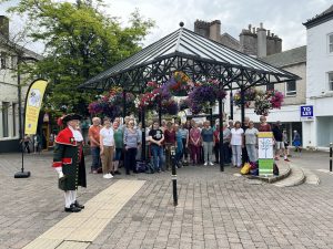 Group of singers gathering under a metal structure to busk alongside the Kendal Town Crier
