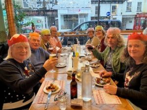 Diners enjoying a tapas Christmas meal together, a few are wearing colourful paper hats