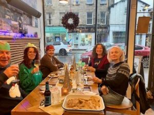 Diners enjoying a tapas Christmas meal together, a few are wearing colourful paper hats