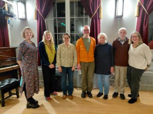 6 smiling performers standing in a semi circle with curtained windows in the background